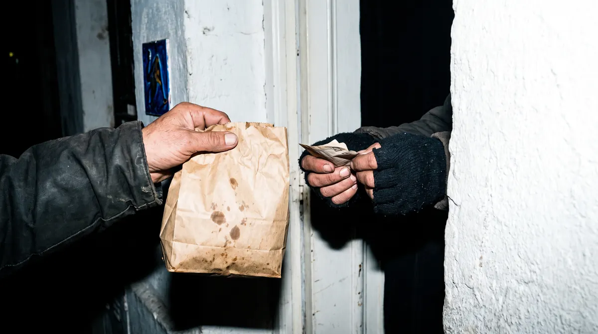 Dos manos en una puerta: una da billetes, la otra una bolsa de empanadas
